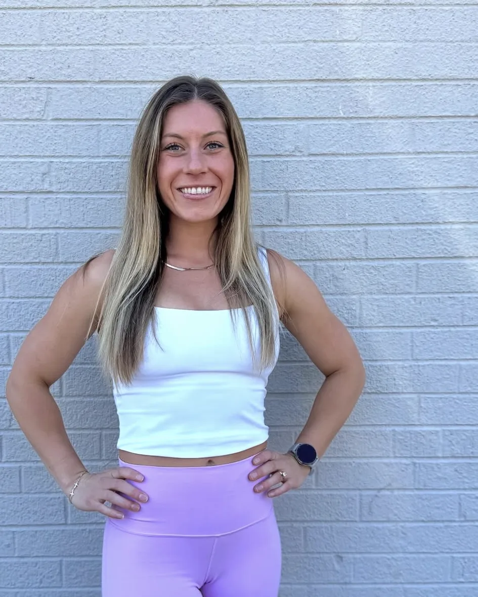 Kenzie Damm, registered dietitian and personal trainer, standing against a white brick wall in Denver