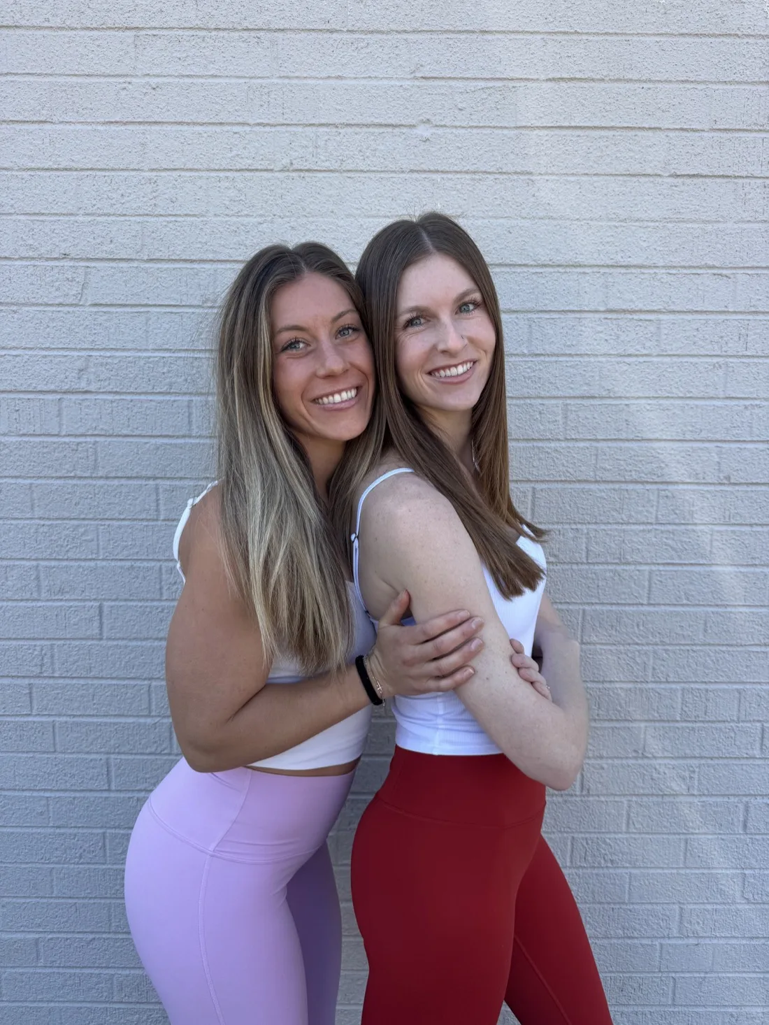 Two Sculpt Social trainers in workout clothes against a white brick wall in Denver