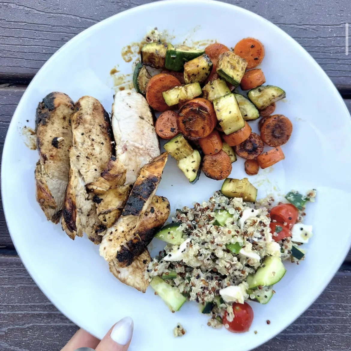 A plate of grilled chicken, roasted zucchini and carrots, and a quinoa salad with cucumber, tomato and mozzarella